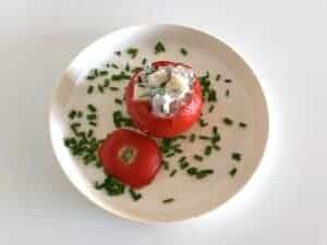 Polish cold stuffed tomatoes topped with cheese and chives on a white plate.