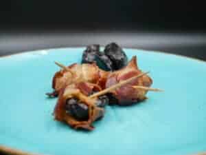 Bacon wrapped prunes on a blue plate.