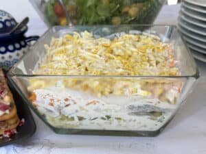 A glass dish brimming with Polish Herring Salad, this recipe features layers of vibrant salad crowned with finely grated egg.