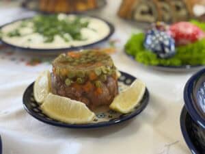 A zimne nogi recipe-inspired gelatin dish features peas and carrots, elegantly garnished with lemon wedges on a plate.