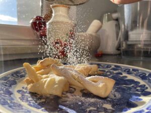 A person is sprinkling sugar on a Polish angel wings recipe.
