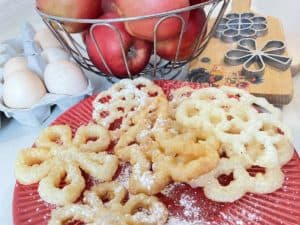 A red plate with a basket of apples, doughnuts, and Polish fried rosette cookies.