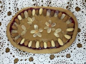 Oval cookie with nut butter, surrounded by almonds and hazelnuts, adorned with almond and hazelnut flowers on a lace doily&mdash;a delightful modern twist reminiscent of Polish caramel Mazurek.