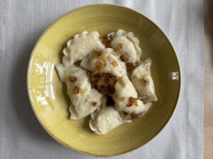 A yellow plate with several boiled dumplings topped with saut&eacute;ed onions, featuring a classic Sauerkraut And Mushroom Pierogi Recipe, placed on a white tablecloth.