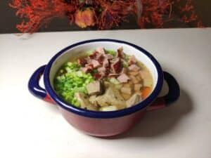 A bowl of Polish ham soup with meat and vegetables in it.