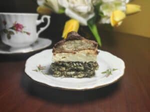 A piece of cake on a plate next to a cup of tea.