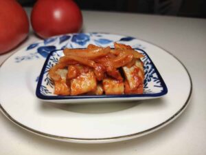 A plate of tofu garnished with Polish herring in tomato sauce, served on a blue and white plate.