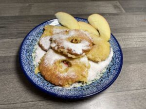 A plate with powdered sugar-dusted Polish apple pancakes without yeast and apple slices.