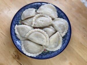 A blue-patterned plate on a wooden table holds a collection of boiled dumplings, showcasing the delicious essence of Pierogi z Mięsem.