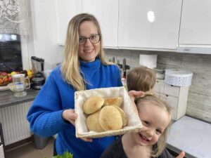 Woman in blue sweater holding a plate of Polish bread rolls with two children in the kitchen.