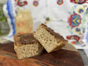 Freshly baked Polish Sauerkraut Bread on a wooden board with a jar of spread in the background.