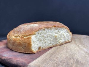 A loaf of Polish potato bread with one end sliced, showing the texture of the crumb, on a wooden cutting board with a dark background.
