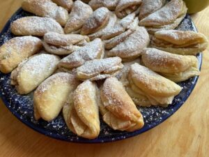 A blue plate topped with numerous folded Polish Apple Cookies dusted with powdered sugar, placed on a wooden table.