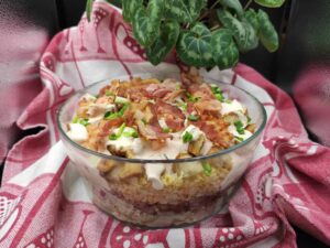 A glass bowl filled with Lumberjack Salad, including rice and toppings, on a red and white cloth.