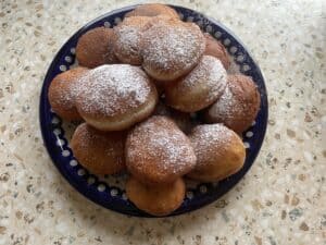 A plate of sugar-dusted vegan pączki on a patterned blue dish rests elegantly on a speckled countertop.
