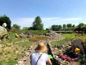 Visiting Magiczne Ogrody, a person in a straw hat enjoys a small train ride winding through stone paths, vibrant flowers, and colorful garden gnome statues in this enchanting Fun Park.
