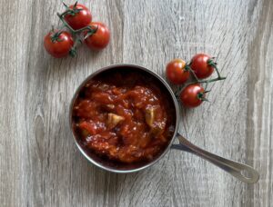 A saucepan filled with tomato sauce, perfect for Polish Leczo or a hearty sausage stew, sits on a wooden surface next to two vine clusters of fresh tomatoes.