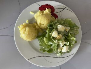 A plate with two scoops of yellow mashed potatoes and a Polish egg and lettuce salad with chopped hard-boiled eggs.
