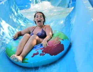 A woman in a swimsuit rides an inflatable tube down a blue water slide at one of Poland&rsquo;s exciting water parks, smiling with her mouth open.