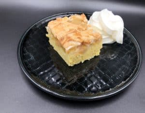 A delicious Polish Rhubarb Cake Recipe served on a black plate with a dollop of whipped cream.