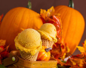 homemade-ice-cream-ideas-for-thanksgiving-image-3-pumpkin-ice-cream-in-cones-with-two-large-pumpkins-and-autumn-leaves-frosted-fusions
