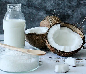 homemade-coconut-ice-cream-recipe-image-3-two-halves-of-a-coconut-with-pieces-scattered-a-jar-of-coconut-milk-and-dried-coconut-pieces-in-glass-dish-with-wooden-spoon-frosted-fusions