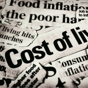 Close-up of torn newspaper headlines focused on “Cost of living” and economic topics like inflation and food prices.