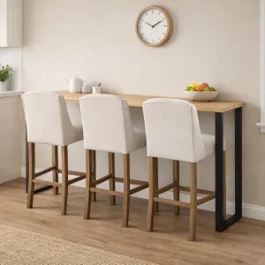 Solid ash breakfast bar with black metal legs and three upholstered bar stools placed against a wall in a modern family kitchen dining area