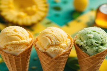 Rum-In-The-Sun-–-Caribbean-Inspired-Ice-Cream-Recipes-Featured-Imaeg-3-ice-cream-cones-with-tropical-background-with-fresh-pineapple-mango-and-coconue-and-a-botlle-of-Rum-Frosted-Fusions