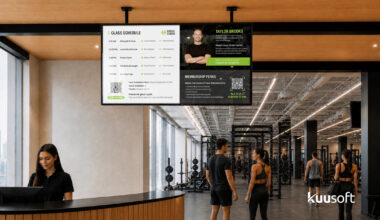 Modern gym lobby with digital displays showing class schedules and member achievement spotlights