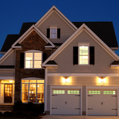 Two-story modern home with lit windows and garage at dusk in a suburban neighborhood