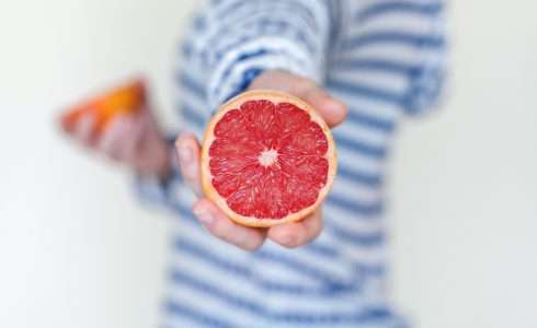 Person in a striped shirt holding a sliced grapefruit with a blurred background, symbolizing functional medicine's focus on nutrition.