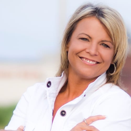 Shannon Barnum, licensed real estate agent, smiling in a white jacket with a blurred outdoor background.
