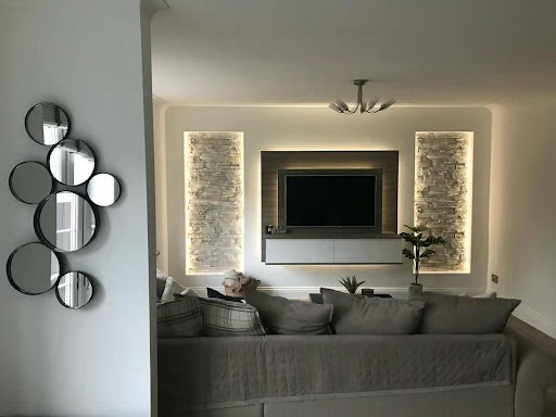 A media wall in a home. There is a couch in front and decorative wall lighting at either side.
