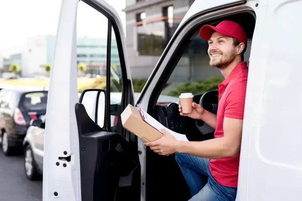 Friendly delivery driver in red uniform takes a coffee break in bustling urban setting.