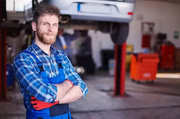 Skilled mechanic in blue overalls confidently oversees repairs in a bustling auto shop.