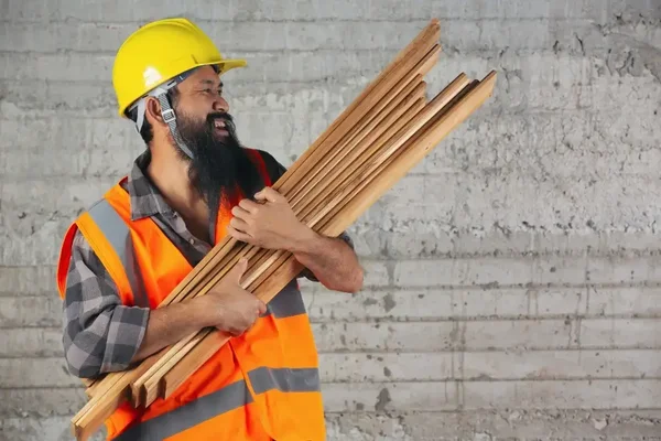 Dedicated construction worker carrying wooden planks, showcasing strength and commitment on-site.
