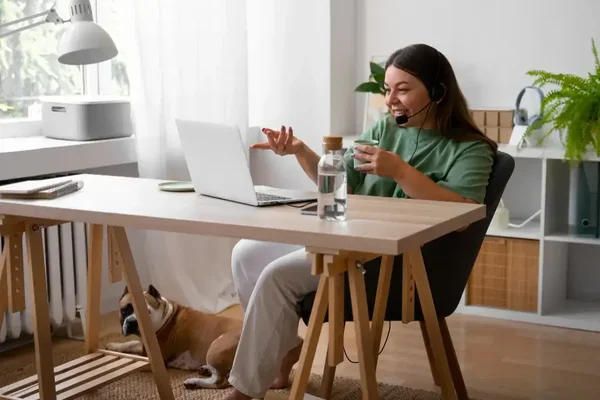Young woman in green sweater engaged in virtual meeting in a cozy, sunlit home office.
