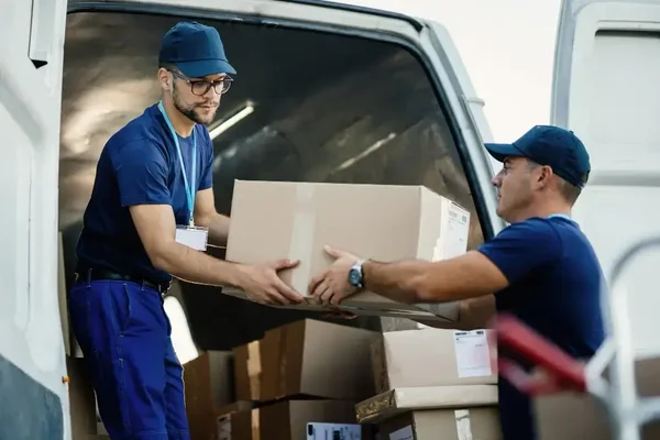 Delivery workers demonstrate teamwork while unloading boxes from a van in a vibrant setting.