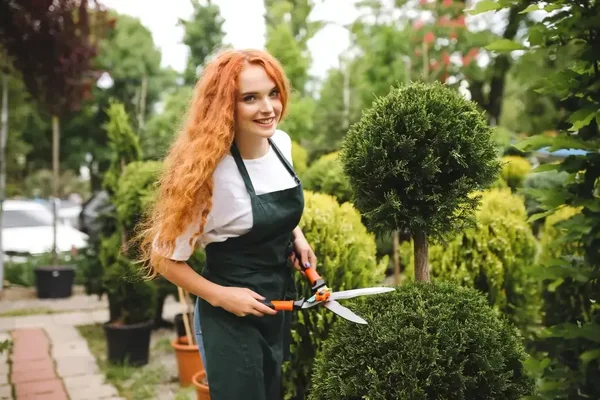 Joyful gardener with red hair skillfully pruning topiary in a lush, vibrant garden.