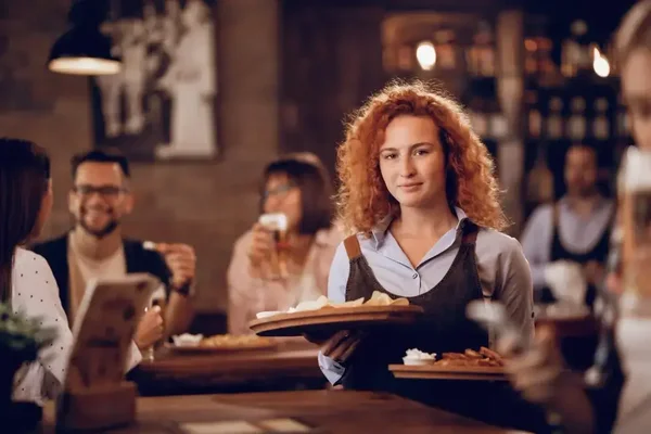 Cheerful server in a cozy restaurant, patrons enjoying lively conversations over delicious meals.