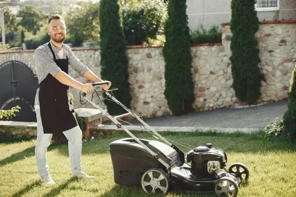 Cheerful man mowing a vibrant lawn, enjoying garden care in warm afternoon light.