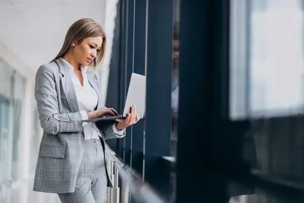 Young professional woman in gray suit working intently on laptop in bright office.