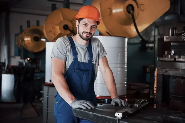 Young worker in safety gear, engaged in industrial workshop tasks surrounded by machinery.