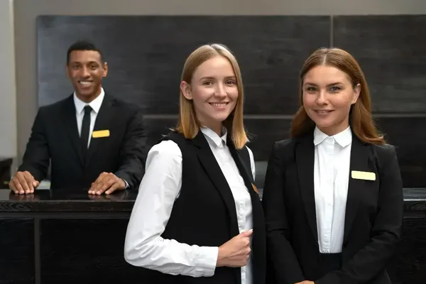 Professional hotel staff exude warmth and friendliness at a modern reception desk.
