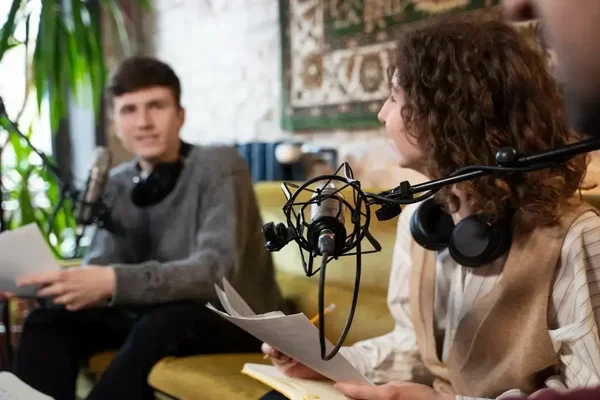 Podcast hosts discuss ideas on a cozy yellow couch in a welcoming, stylish setting.