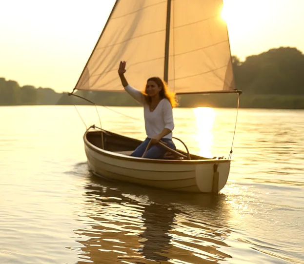 Eine junge Frau in einem Segelboot mitten auf dem Fluss steuert. Die Abendsonne spiegelt sich golden im Wasser.