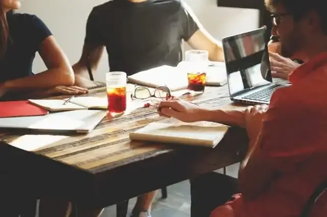 Team meeting around table with laptops and notepads.