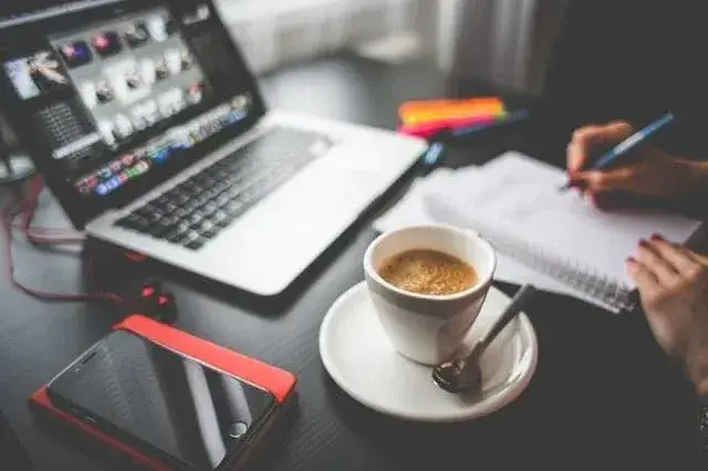 Cozy creative workspace with laptop, coffee, notepad, and colorful highlighters in natural light.