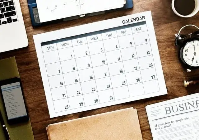 Organized workspace with calendar, laptop, clock, and newspaper for effective productivity and time management.